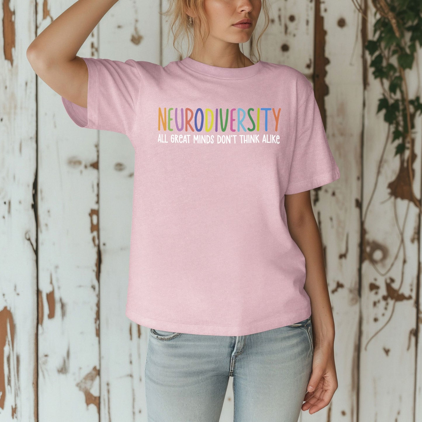 Person wearing a pink t-shirt with 'NEURODIVERSITY ALL GREAT MINDS DON'T THINK ALIKE' text against a wooden background.
