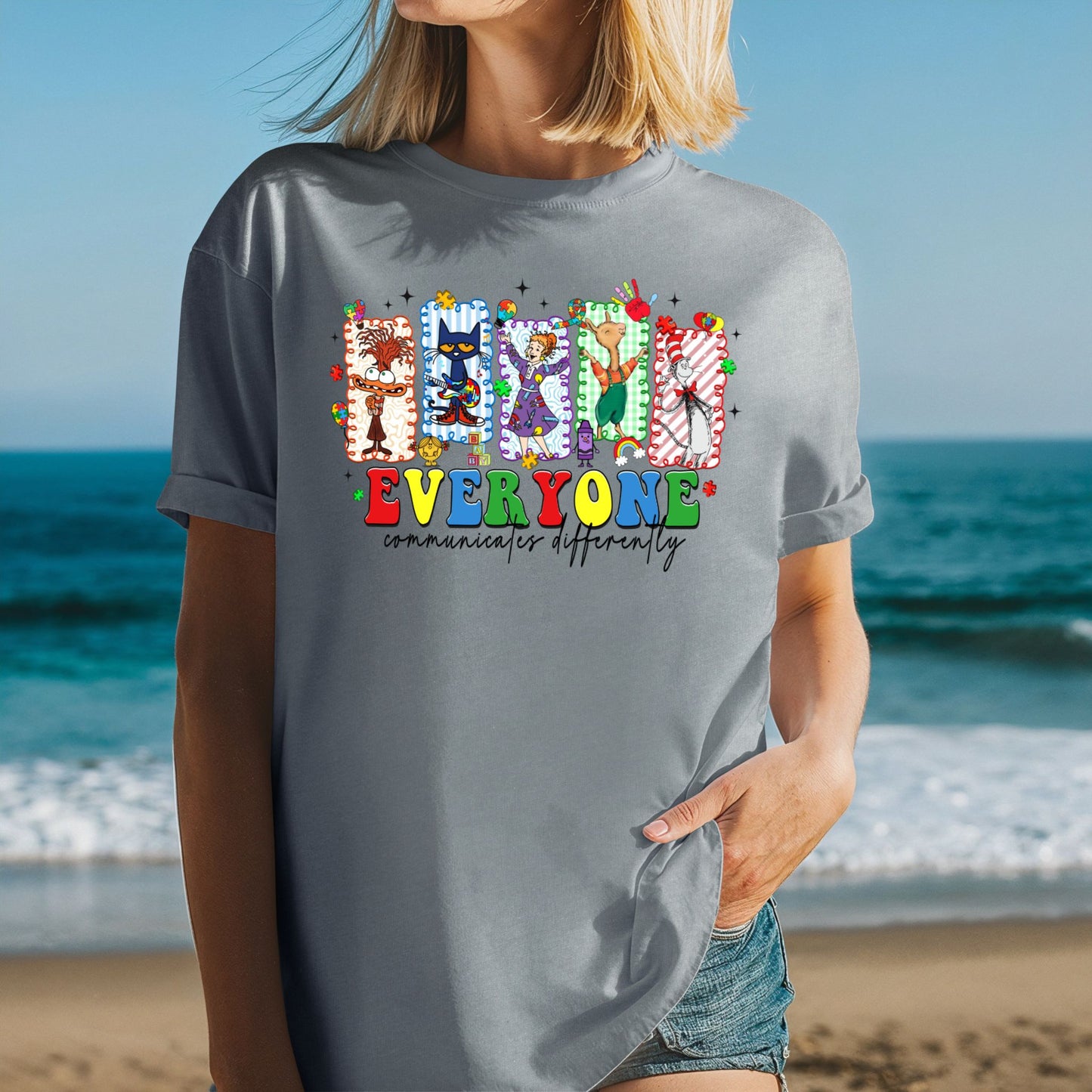 Person wearing a gray t-shirt with colorful graphic and text on a beach