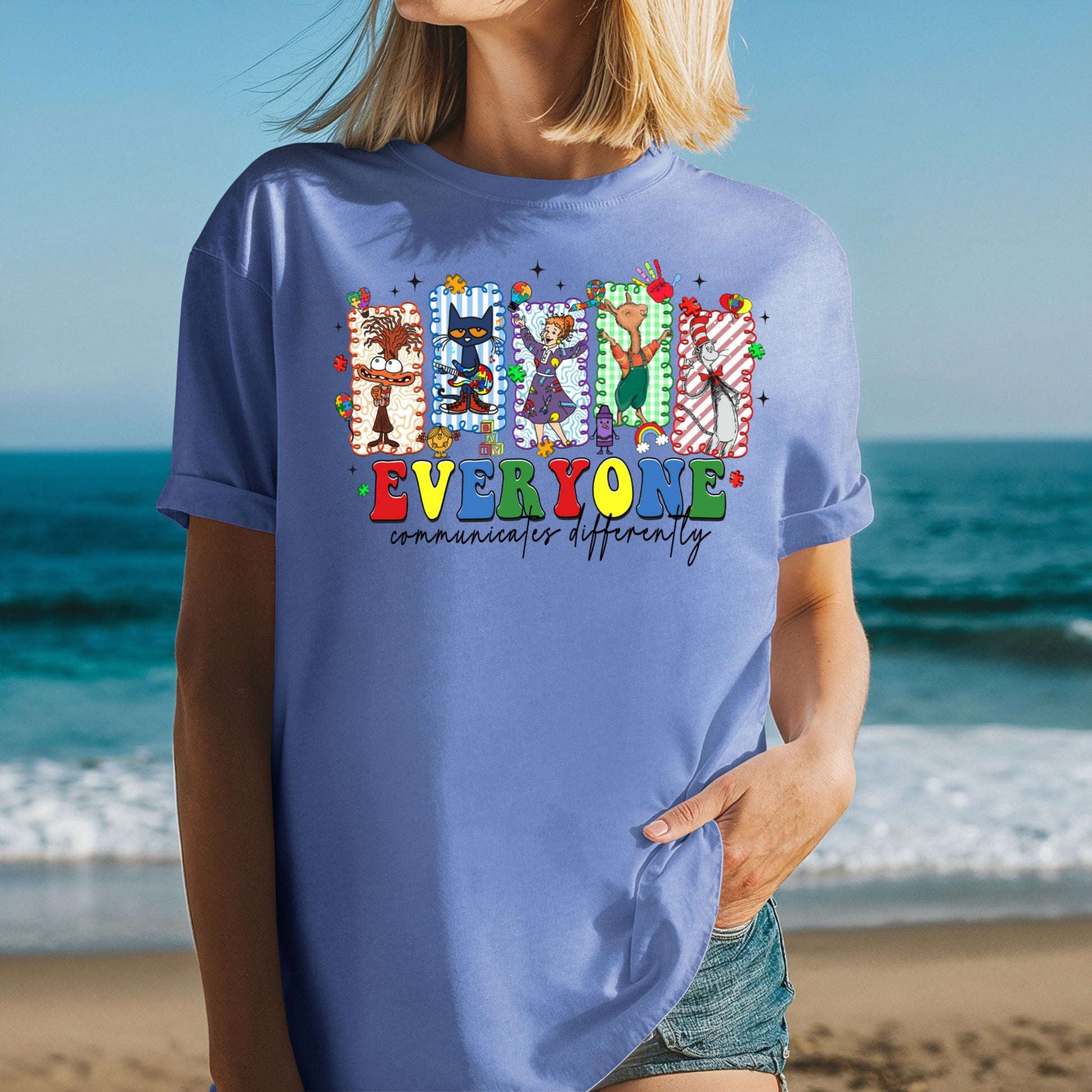 Person wearing a blue t-shirt with colorful graphics and text on a beach.