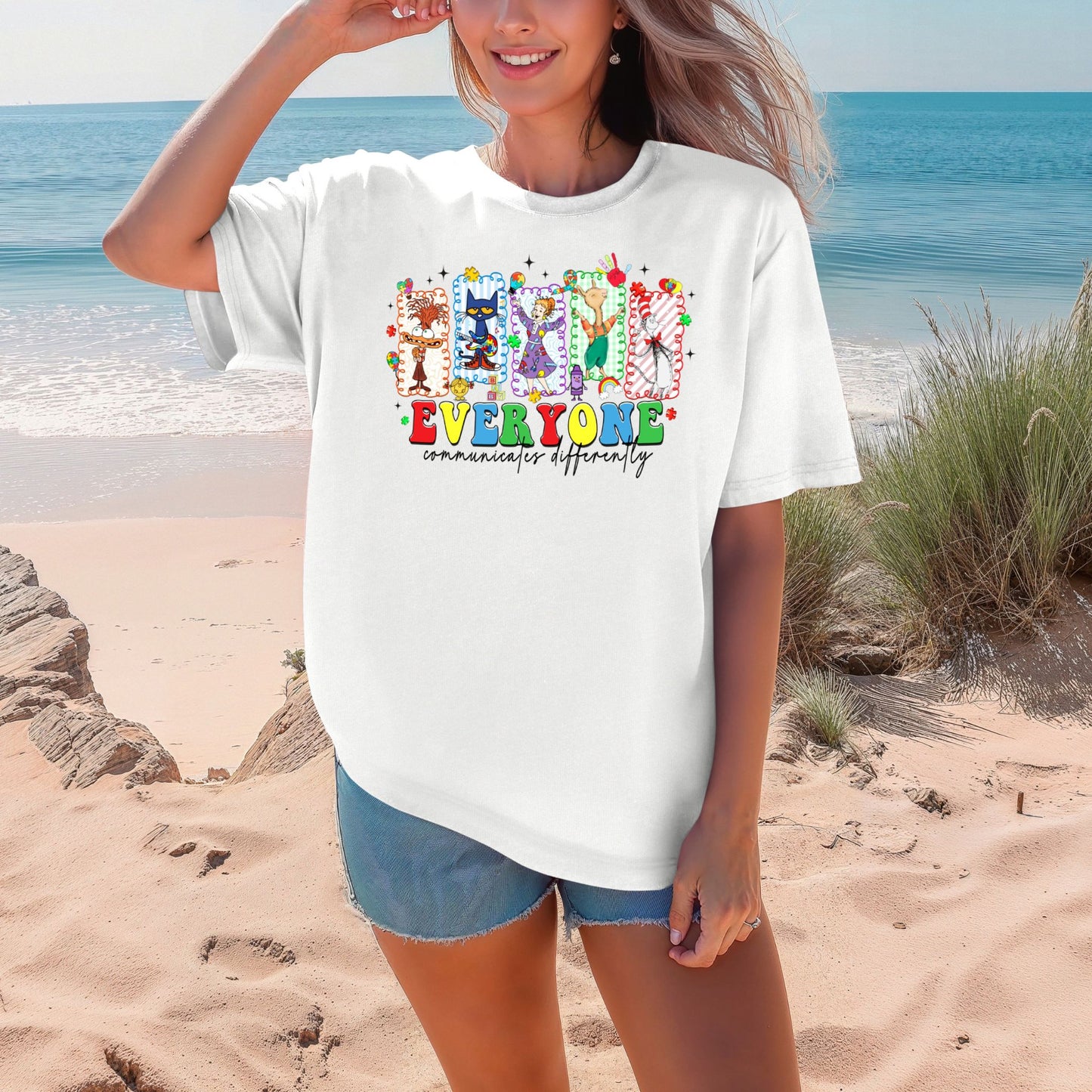 Person wearing a white t-shirt with colorful graphics and text on a beach.