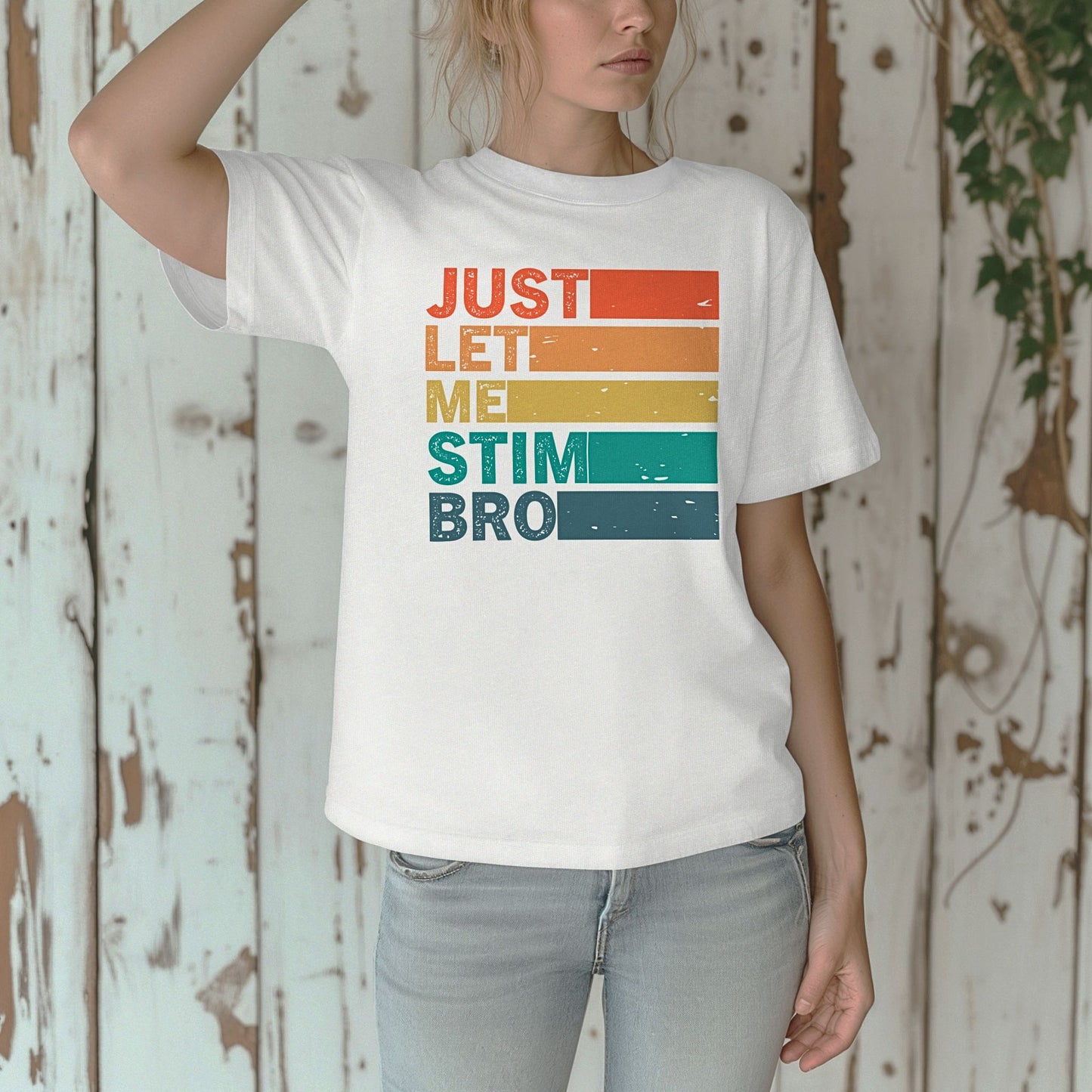 Woman against a rustic white wooden wall wearing a White Comfort Colors t-shirt. The shirt features bold retro stripe lettering reading Just Let Me Stim Bro stacked vertically with each word on a colored stripe in orange, peach, yellow, teal, and dark teal with a distressed vintage texture.